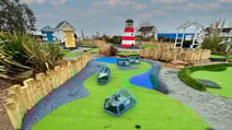 A colorful mini-golf course featuring striped lighthouse, beach huts, and vibrant landscaped areas with paths and obstacles at Corton