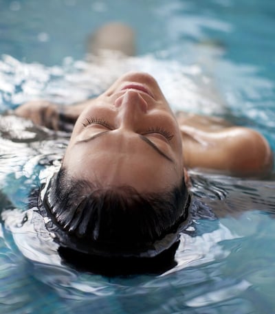 Tranquil woman, eyes closed, floating in a pool at Heythrop Park Hotel, embracing the soothing ambiance of the water.