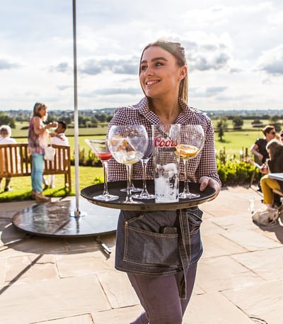 A team member carrying empty drinks glasses on a tray during the Gin Festival